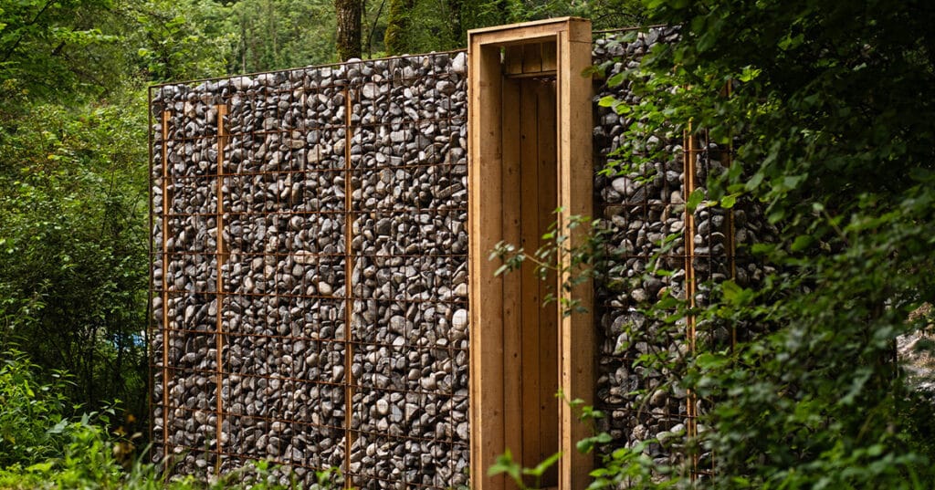 gabion walls frame tephra’s stone shelter along dry riverbed in french mineral landscape